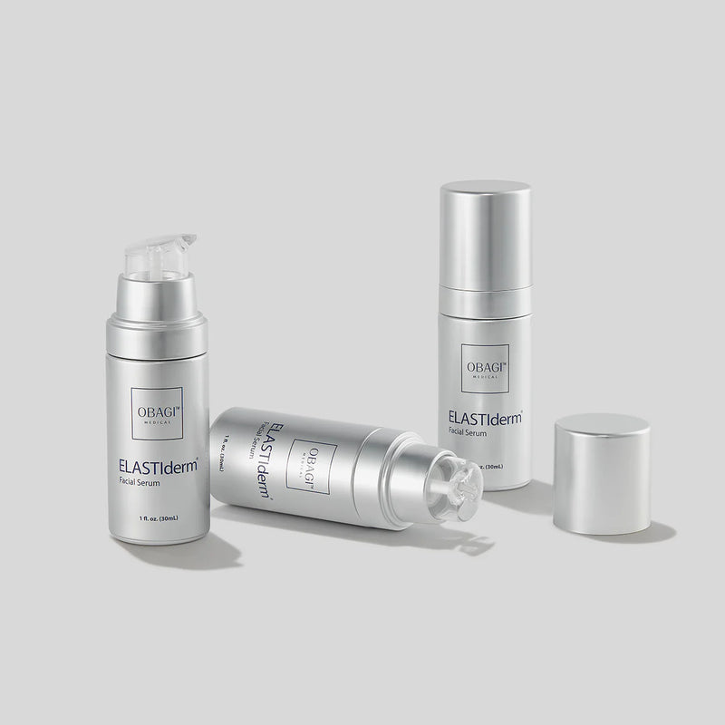 An image of three bottles of Obagi ELASTIderm Facial Serum. Two have  their caps removed. One of the bottle without a cap is lying horizontally on the surface.