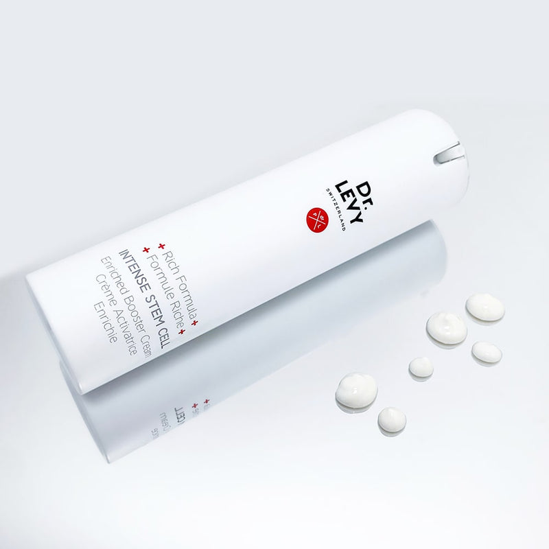 An image of a bottle of Dr Levy Enriched Intense Stem Cell Booster Cream lying vertically on a surface with six droplets of its content beside it.