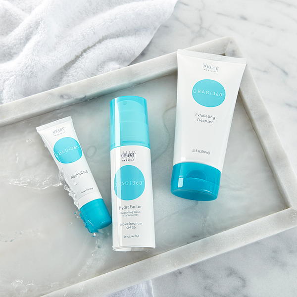 An image of  Obagi Retinol 0.5, Obagi Hydrofactor, and Obagi Exfoliating Cleanser lying horizontally in a tile surface.